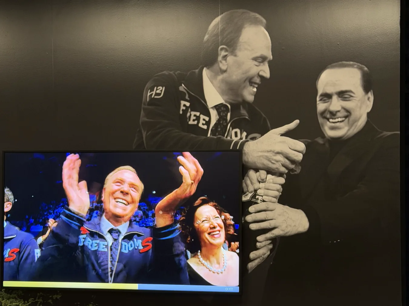 Screen at Mediolanum showing a celebration, next to a black-and-white photo of the founders